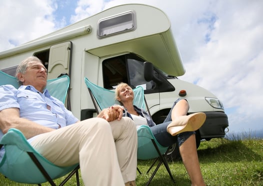 Senior couple relaxing in camping folding chairs, camper in background.jpeg